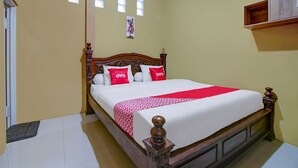 Una cama impecable con cabecera de madera, ropa de cama blanca y almohadas rojas con el texto 