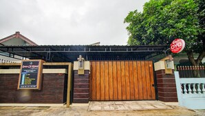 Una entrada cerrada con puerta de madera, un letrero con texto y un árbol al fondo.