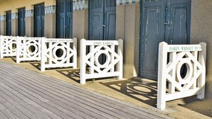 Filas de puertas con nombres en placas blancas, una pasarela de madera y un edificio con un borde de azulejos.