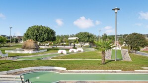 Un campo de mini golf con una estructura de techo de paja, arcos blancos y una palmera.