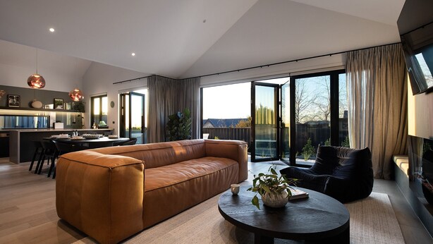 A modern living room with a leather sofa, a round coffee table, and a view of the outdoors through large sliding glass doors.