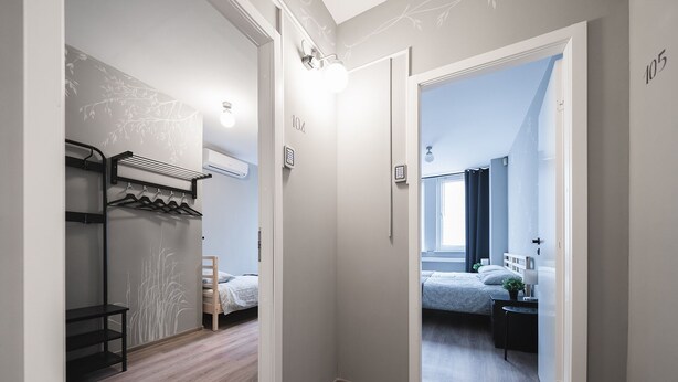 A hallway leading to a bedroom with a bed, a bedside table, and a window. There is a coat rack and a shelf with a hanging item. - Lollo Motel Graičiūno - Lollo Luxury (Vilnius)
