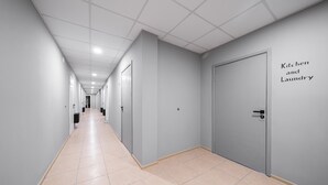 A long, narrow hallway with light-colored walls and a tiled floor, leading to a door labeled "Kitchen and Laundry." - Lollo Motel Graičiūno - Lollo Luxury (Vilnius)