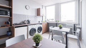 A modern kitchen with a dishwasher, washing machine, and a microwave. There is a dining table with chairs and a potted plant. - Lollo Motel Graičiūno - Lollo Luxury (Vilnius)