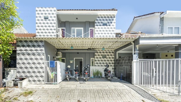 A building with a geometric facade, a covered entrance, and a gated parking area with motorcycles. - OYO Life 3782 Gunung Anyar (Surabaya)
