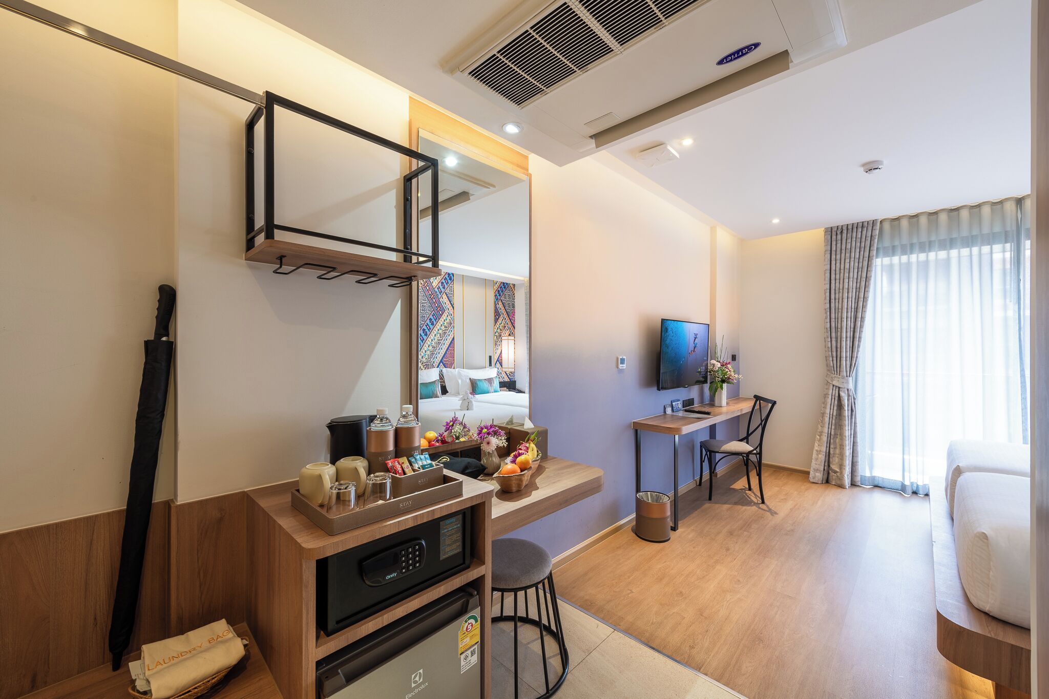 A modern hotel room with a wooden desk, a flat-screen TV, a comfortable bed, and a large mirror.