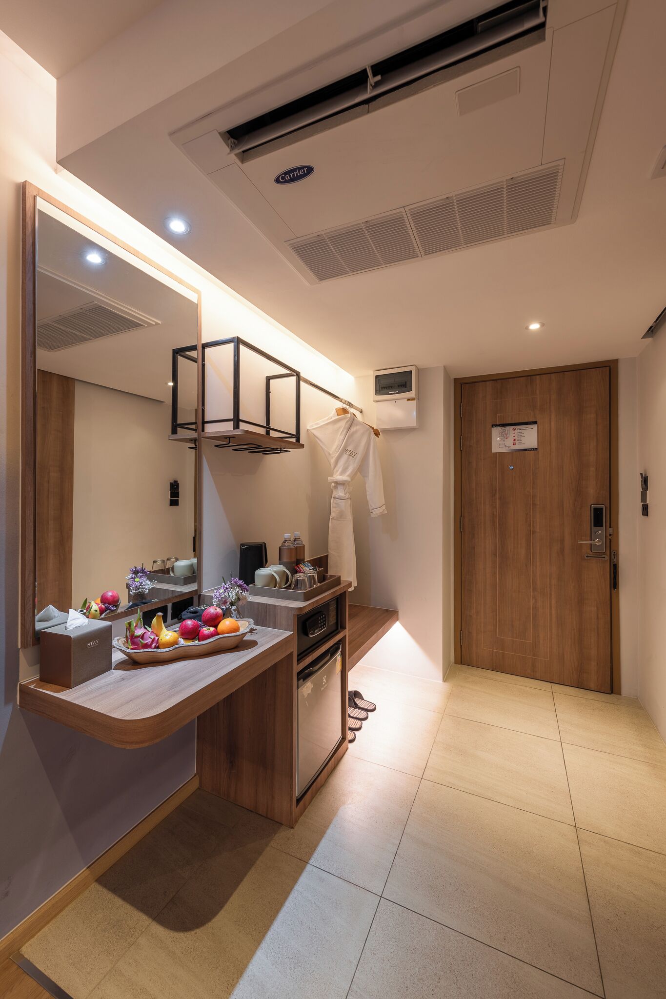 Une chambre d’hôtel avec une coiffeuse en bois, un grand miroir, une porte en bois et un petit téléviseur fixé au mur.