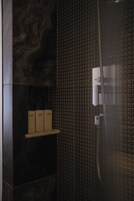A bathroom with dark marble tiles, a textured shower wall, and a small shelf with boxes.