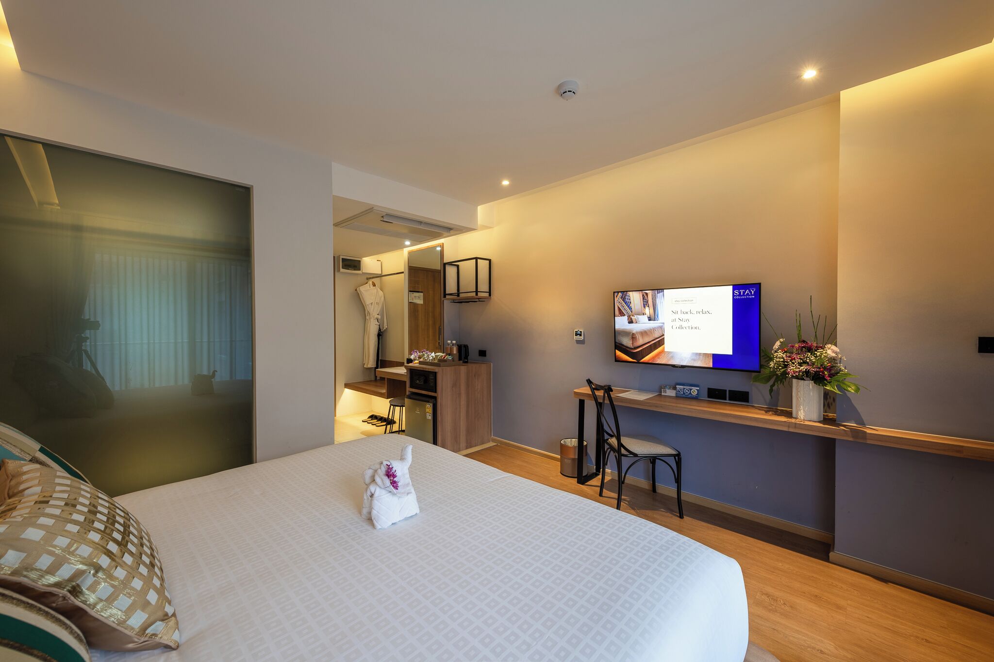 A hotel room with a bed, a desk, a TV, and a bathroom visible through a glass door.