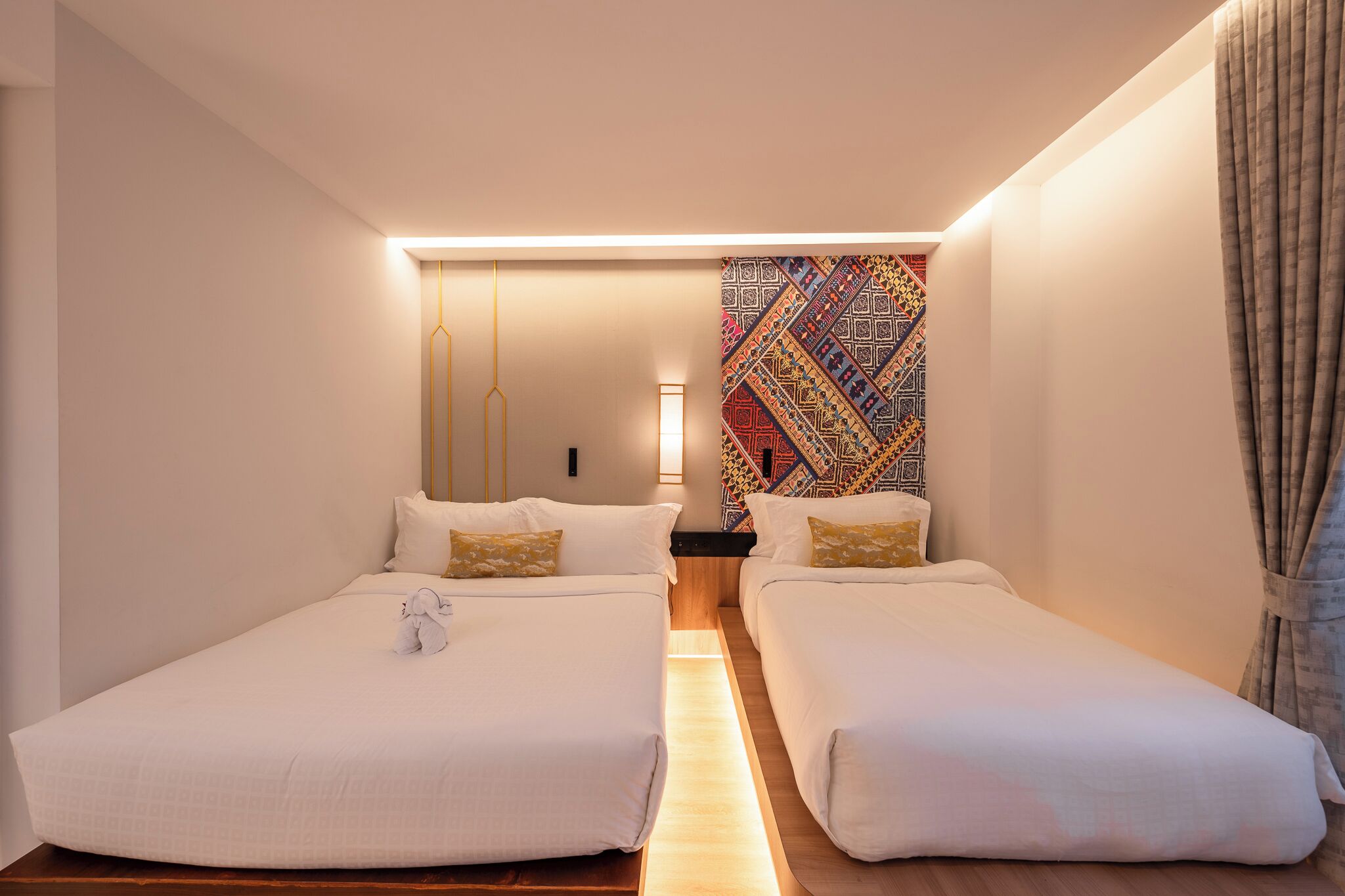 Habitación de hotel con dos camas individuales, una mesita de noche, una lámpara y un tapiz colorido en la pared.