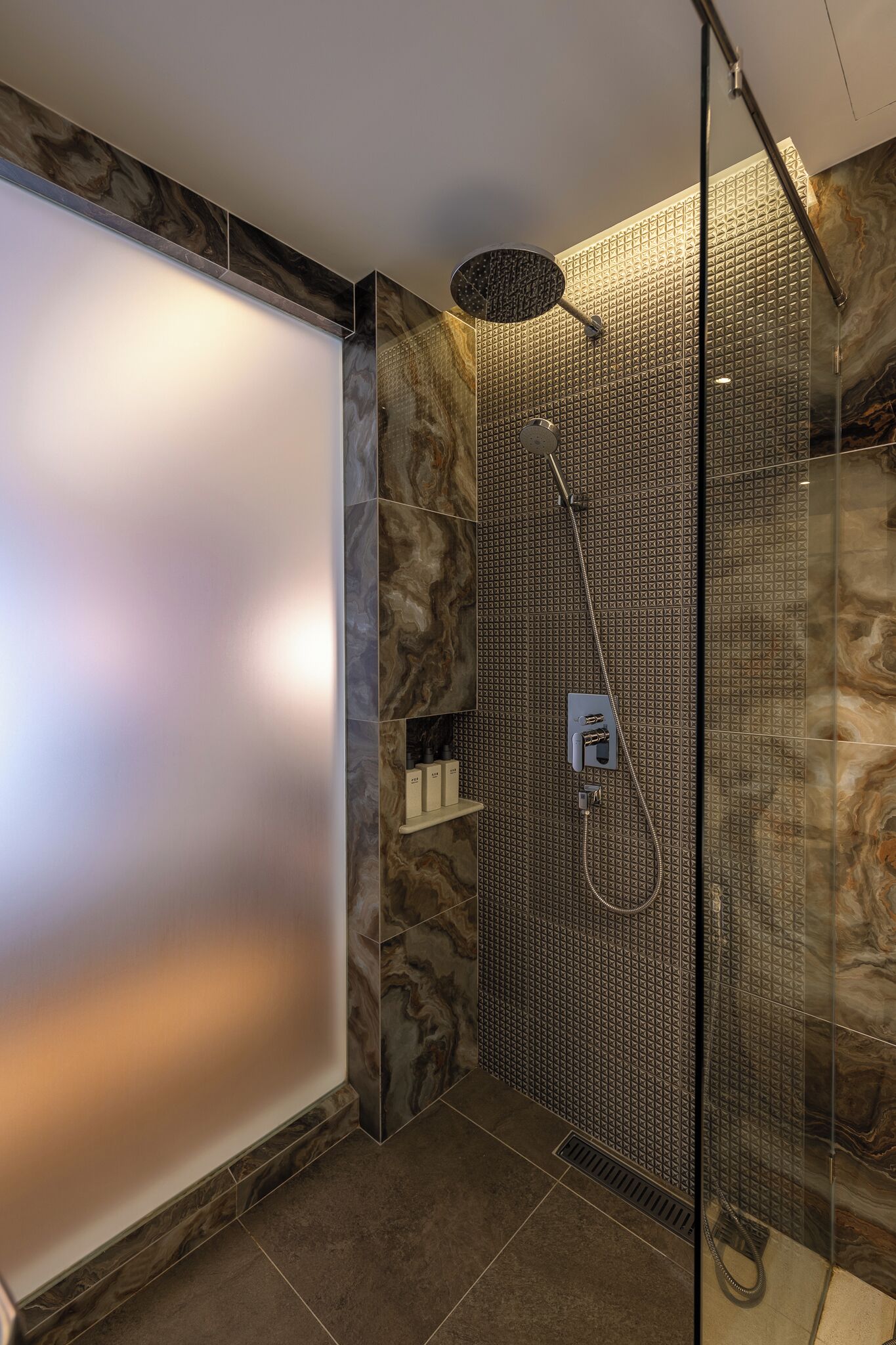 A modern shower with a rain showerhead, a glass enclosure, and a marble wall.