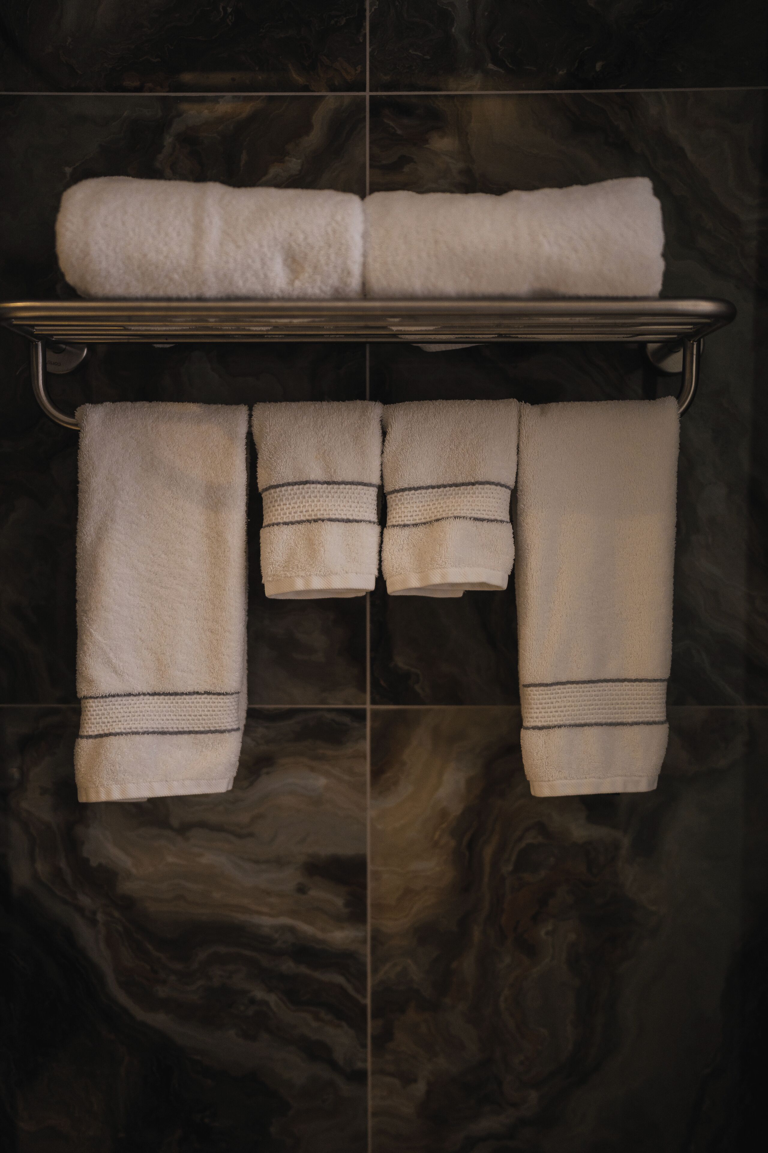 A bathroom with a metal towel rack holding three towels and a folded towel on a shelf.