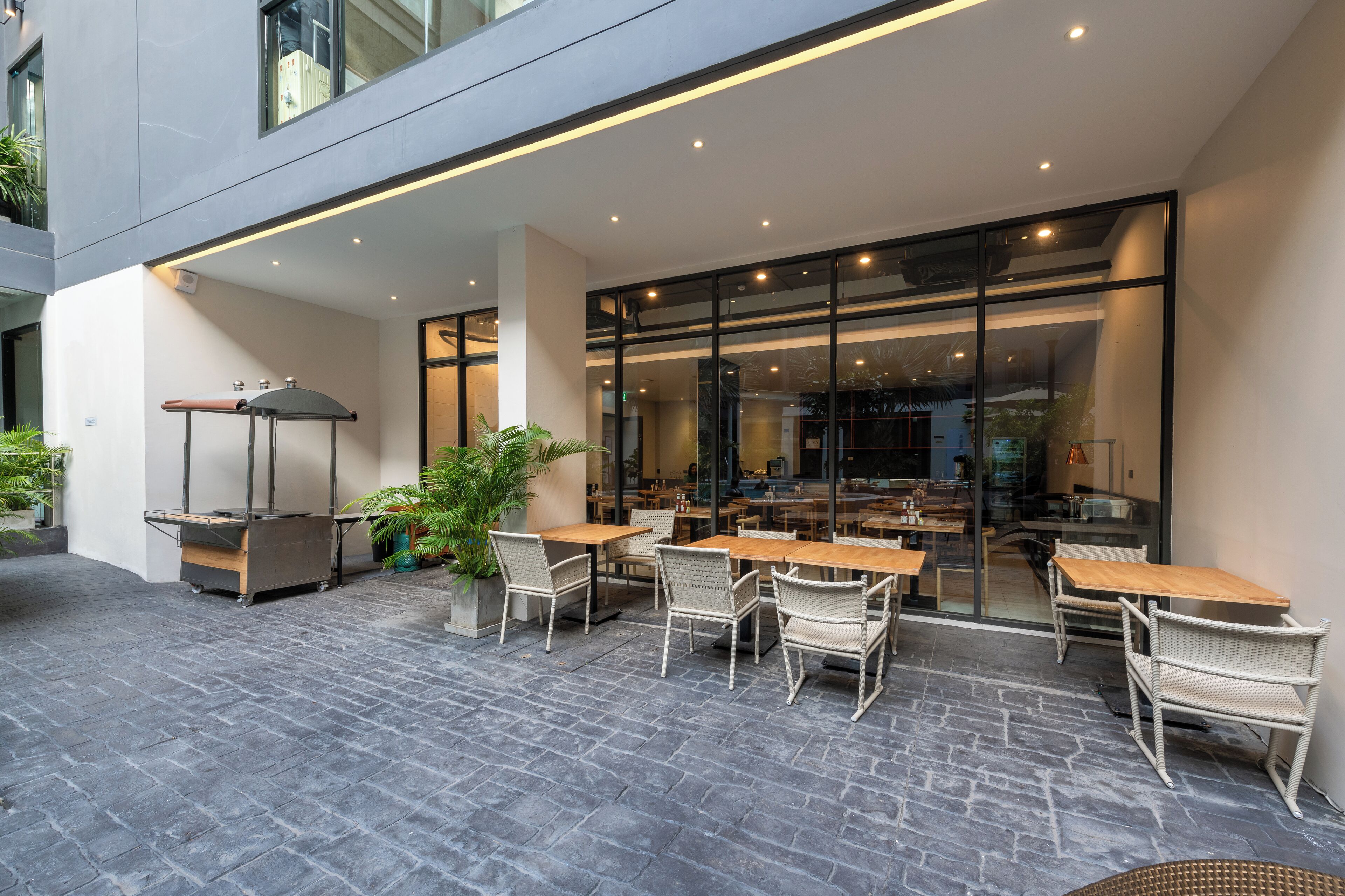 An outdoor patio with tables and chairs, a potted plant, and a glass door leading to an interior space.