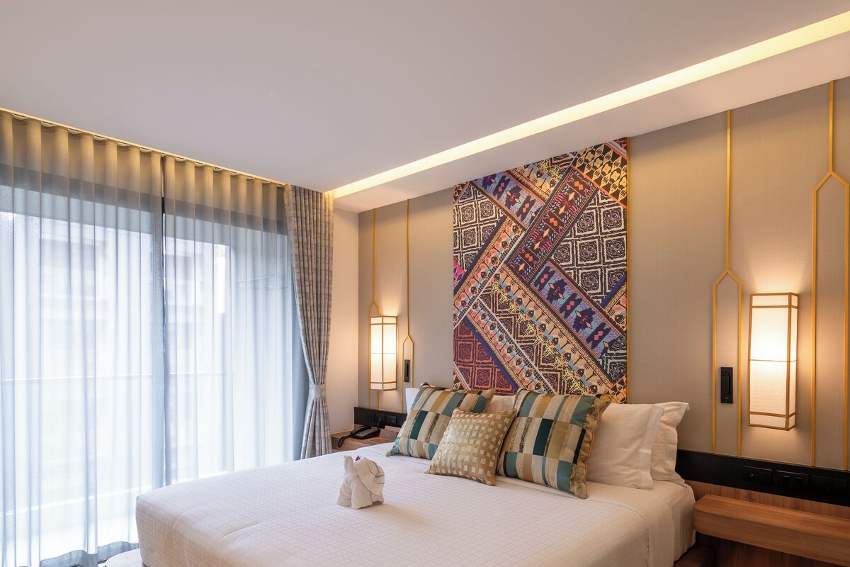 A modern hotel room with a large bed, wooden platform, patterned wall art, and ambient lighting.