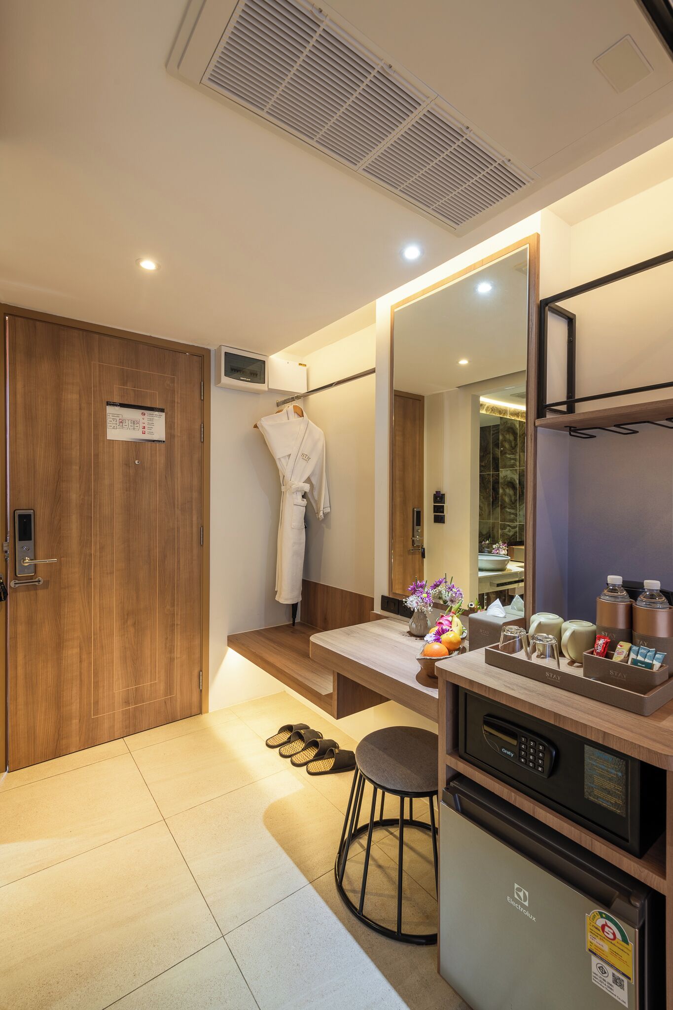 Ein modernes Badezimmer mit Holztür, einem aufgehängten Bademantel, einem Waschbecken, einem Spiegel und einem kleinen Kühlschrank.