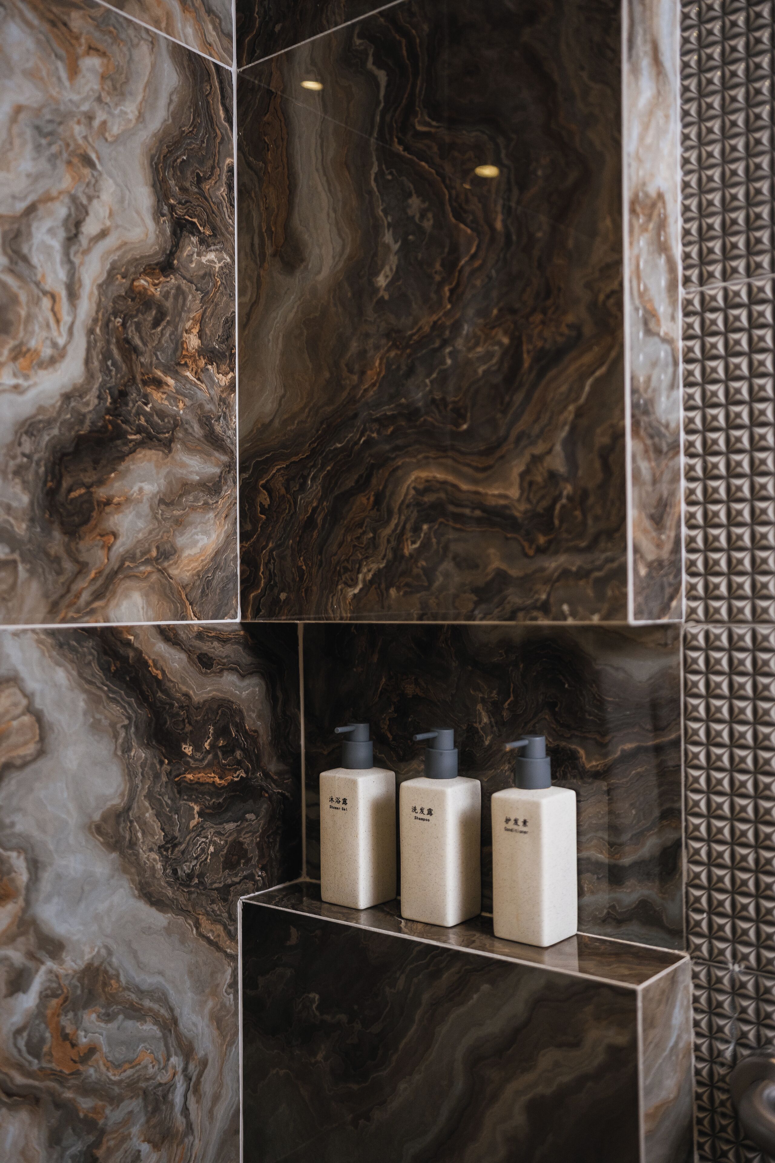 A bathroom with marble tiles and three toiletries on a shelf.