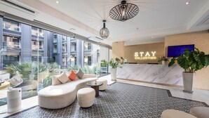 Um hall de hotel moderno com balcão de recepção, um conjunto de sofás, piso estampado e grandes janelas com vista para a paisagem urbana.