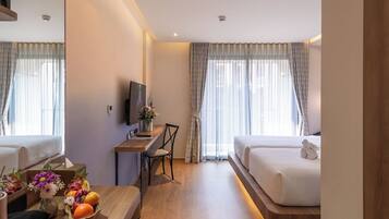 Une chambre d’hôtel avec un lit, un bureau, une chaise, une télévision et une petite table agrémentée de fleurs et de fruits.