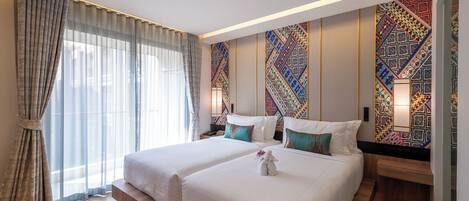 A hotel room with two beds, a large window with curtains, a patterned wall, and a nightstand with a lamp.