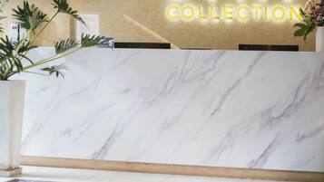 Un área de recepción con un mostrador de mármol, un letrero que dice 'STAY COLLECTION' y una planta pequeña.