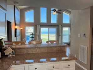 A kitchen with a granite countertop, white cabinets, and a view of the outdoors through large windows. - Sandy Seahorse - 3rd Home From Beach Access! (Galveston)