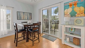A dining area with a table and chairs, a chandelier, a large window with a view, and a shelf with decorative items. - Myrtlewood Resorts Serene Getaway Unit 105 (Myrtle Beach)