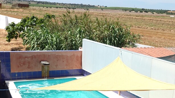 Una persona sentada junto a una piscina con vista a un campo y colinas al lejano.