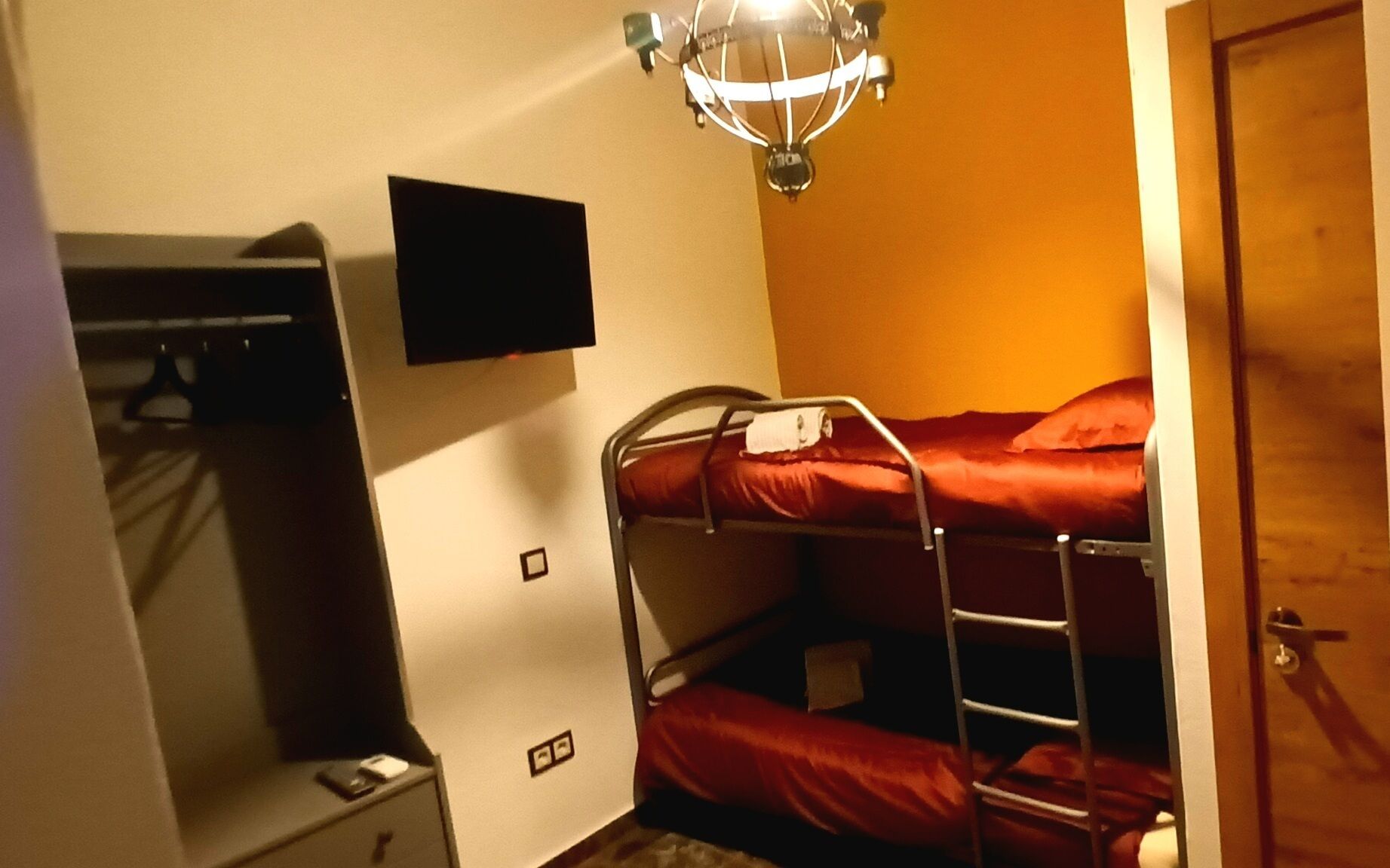 A compact room with a bunk bed, a small desk, a chair, a television, and a door.