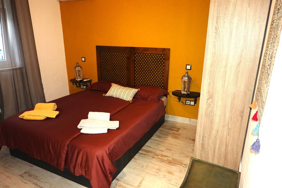 A hotel room with a large bed, two bedside tables with lamps, a wooden headboard, and a yellow wall.