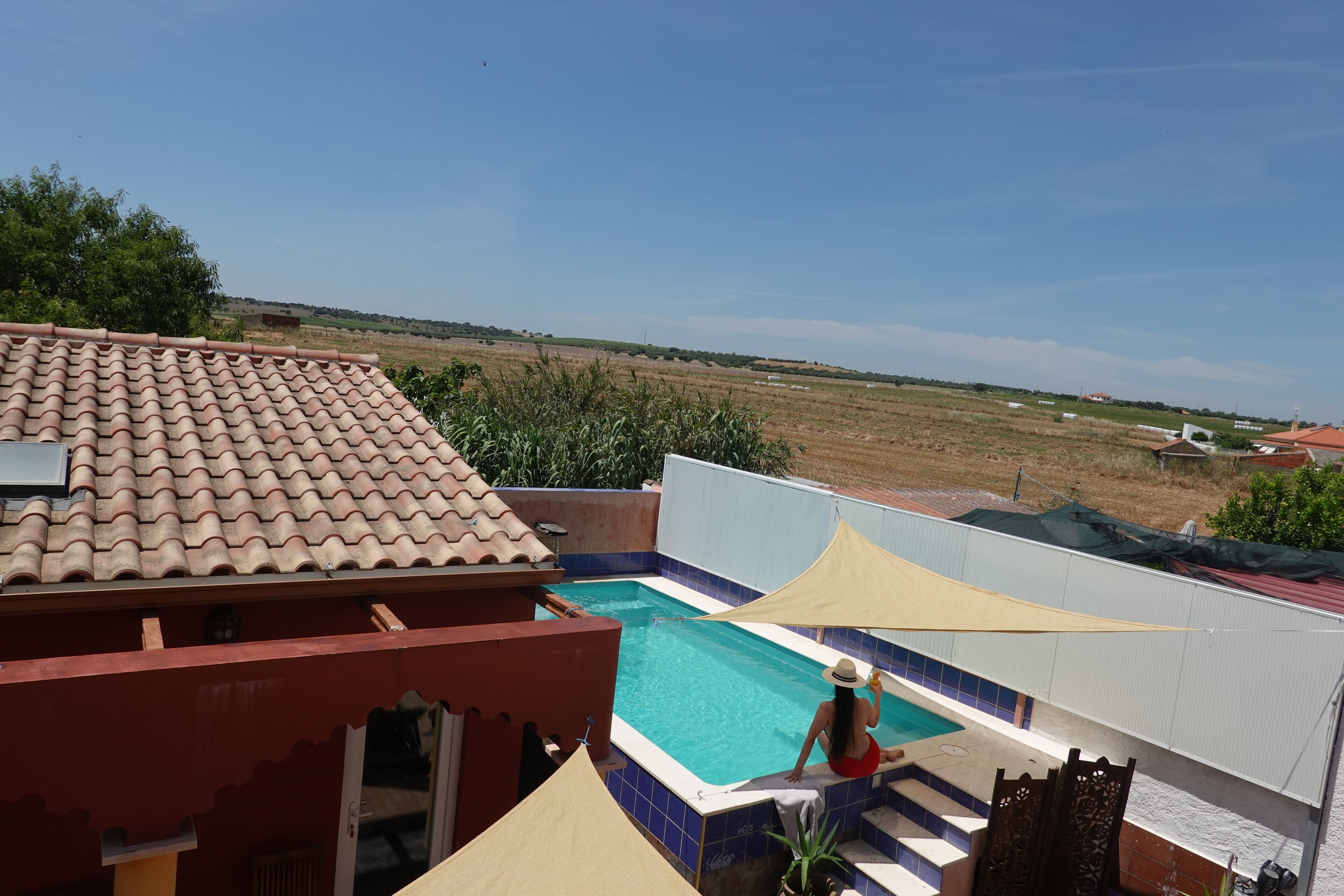 A swimming pool with a view of the countryside, a tiled roof, and a red building.