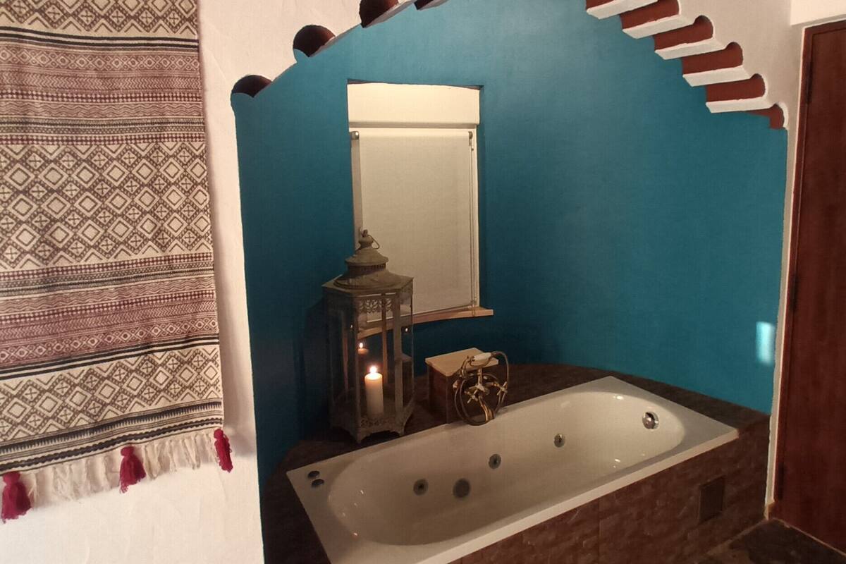 A bathroom with a bathtub, a mirror, a lantern, and a patterned towel.