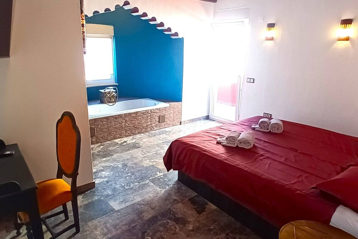 A hotel room with a bed, a desk, a chair, and a bathroom visible through an open door.
