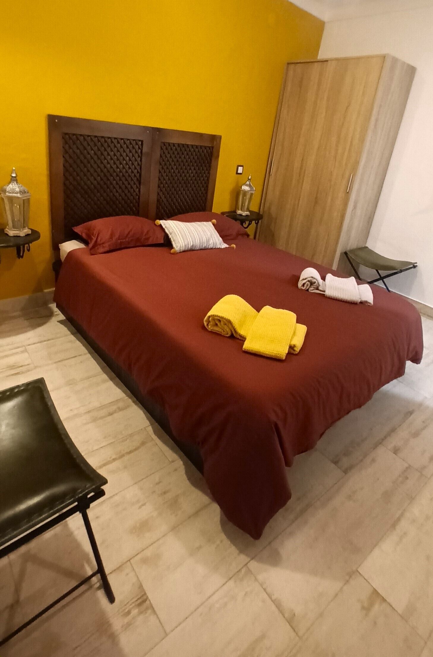 Una habitación de hotel con un armario de madera, una cama con ropa de cama roja y una silla verde.