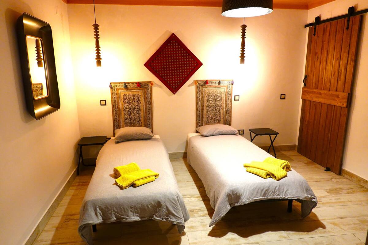 A room with two beds, each with a yellow towel, a mirror, patterned curtains, and a wooden door.