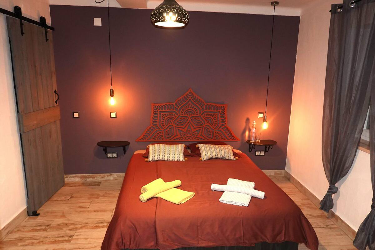 A room with a large bed, two bedside tables, a hanging light fixture, and a decorative wall piece.