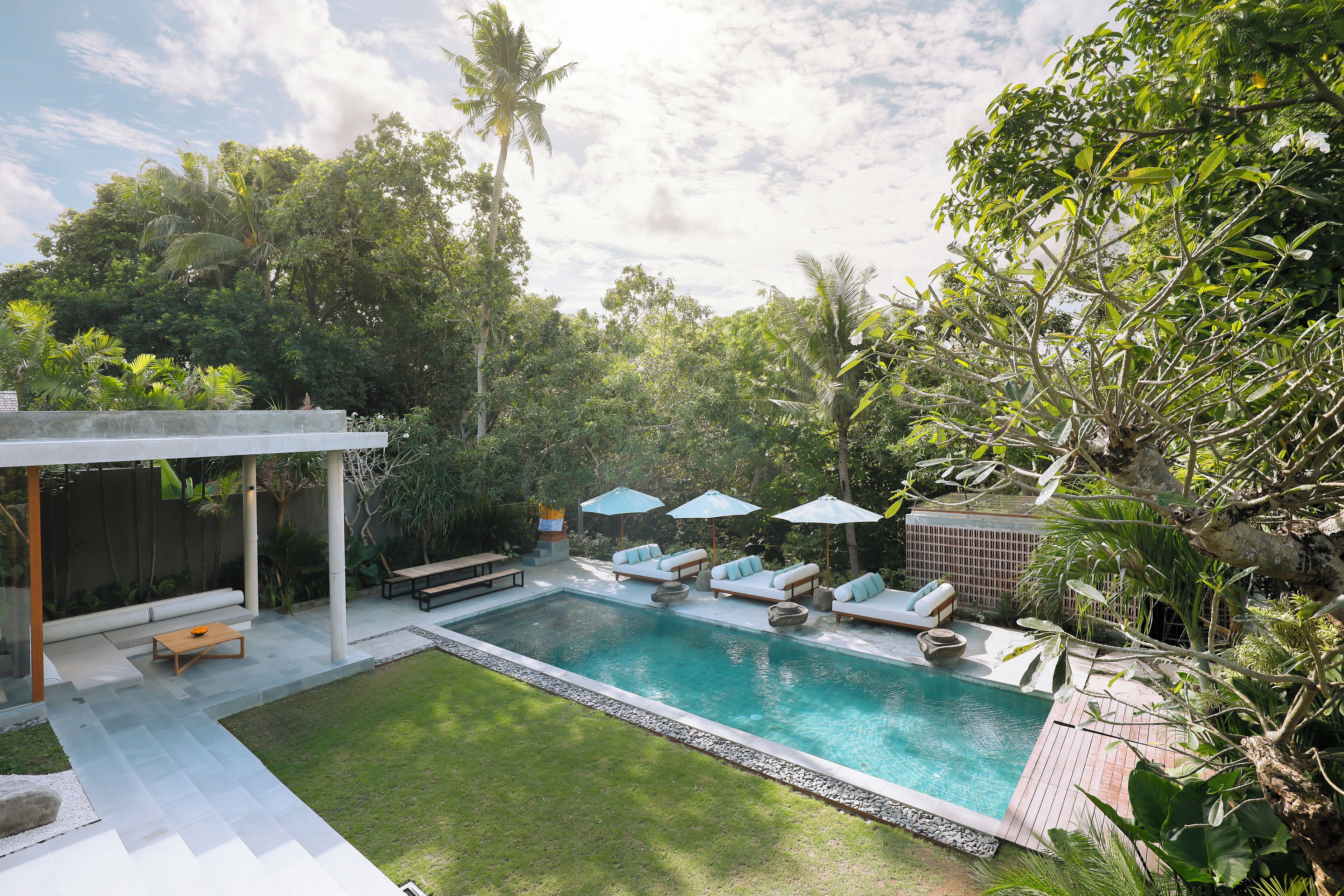 Une piscine entourée de chaises longues et de parasols, le tout bordé d’une végétation luxuriante et d’une pelouse bien entretenue.