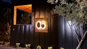 A modern building with a dark facade, a wooden-framed window, and a number '06' illuminated sign.