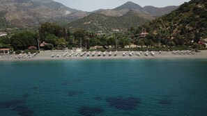 A coastal area with a beach, umbrellas, and a mountainous backdrop.
