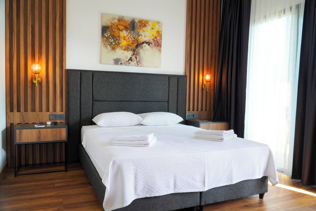 A modern hotel room with a large bed, wooden paneling, and two wall-mounted lamps.