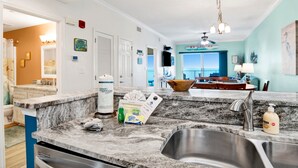 A kitchen with granite countertops, a stainless steel sink, and a dining area with a view. - Direct Gulf Front-Great View-Hot Tub-Swimthru Pool (Gulf Shores)