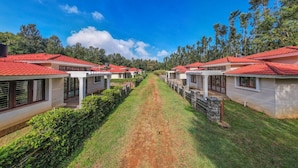 Une rangée de bâtiments de style bungalow, avec des toits recouverts de tuiles rouges, disposés en ligne le long d’un chemin de terre.
