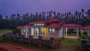 Une maison à deux étages, avec un toit recouvert de tuiles rouges, une clôture en pierre et une cour gazonnée.