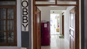 Un corridoio con stipite in legno recante l'indicazione "Lobby", un frigorifero e uno scorcio di una stanza con una sedia gialla e un tappeto verde.