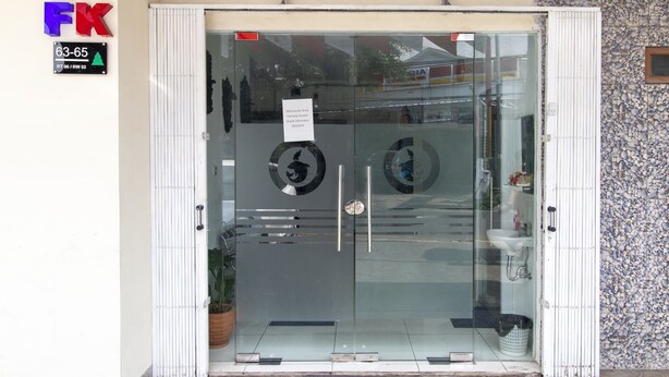Ingresso di un hotel con porta in vetro, una targa che indica i numeri delle stanze 63-65 e un logo con le lettere "FK".
