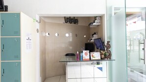 Un'area di accoglienza con un bancone in vetro, un computer, una sedia e un telefono fissato al muro.