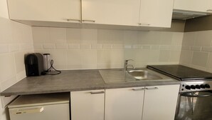 A compact kitchen with white cabinets, a stainless steel sink, a built-in oven, and a dishwasher. - T2 with swimming pool in the heart of the pines (Saint-Julien)
