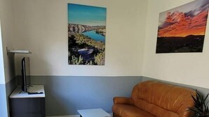 A living room with a glass table, a brown leather sofa, a small white table, and two paintings on the wall. - T2 with swimming pool in the heart of the pines (Saint-Julien)