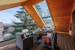A wooden deck with a glass ceiling, wicker furniture, and a view of trees and buildings. - Apartament WATAHA (Zakopane)