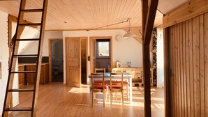Een ruime kamer met houten vloeren, een eettafel met stoelen, een trap en een raam.