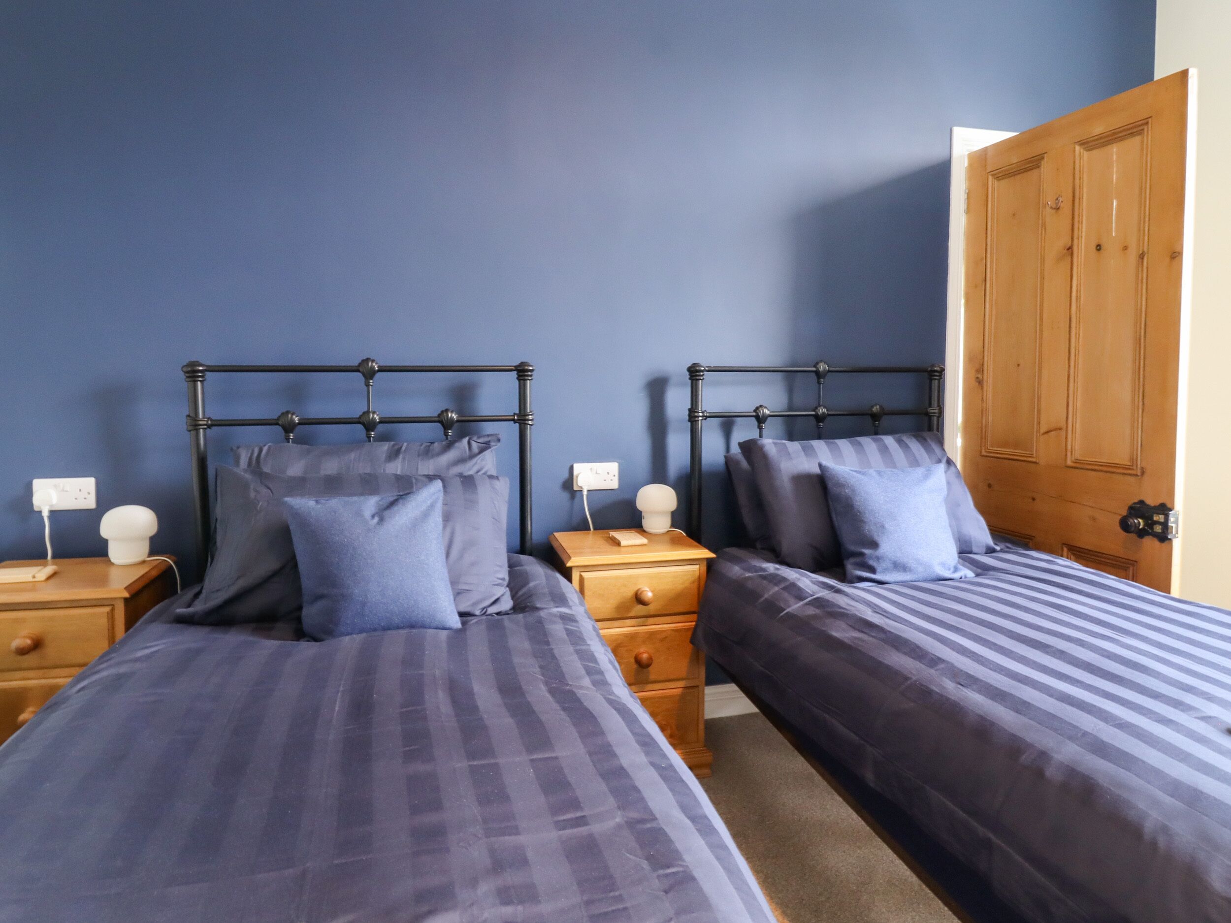 A bedroom with two beds, each with a wooden nightstand and a lamp.